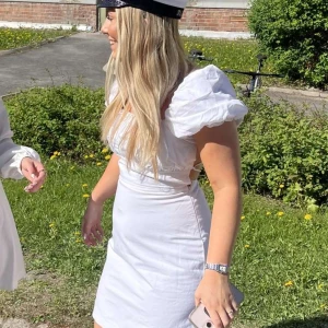 Studentklänning med öppen rygg - Säljer min superfina studentklänning. Den har puffiga kortärmar och en snygg öppen rygg med snörning. Klänningen är tight och kort, vilket gör den perfekt för sommarens festligheter. Materialet känns lätt och bekvämt. Passa på att fynda denna stilrena klänning! 🌸