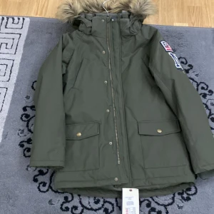 Grön parkajacka  - Säljer en snygg grön parkajacka i storlek 152. Jackan har en mysig pälsfodrad huva och praktiska fickor med knappar. Perfekt för kalla höst- och vinterdagar. Den har en dragkedja framtill och är i mycket bra skick. Passar både till vardags och lite finare tillfällen.