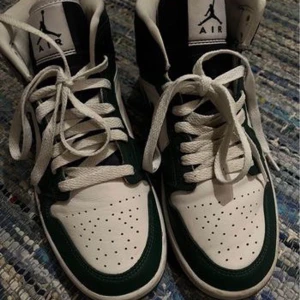 Nike Air Jordans i grönt och vitt - Säljer ett par snygga Nike Air Jordans i grönt och vitt. Skorna har en klassisk hög modell med snörning och perforerade detaljer på tån för extra ventilation. De är i bra skick och perfekta för både vardag och fest. Passar dig som vill ha en stilren och sportig look.