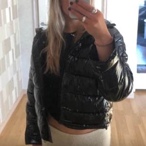 Svart glansig pufferjacka - Svart glansig pufferjacka från zara. Jackan har en croppad passform och långa ärmar. 💕storlek s