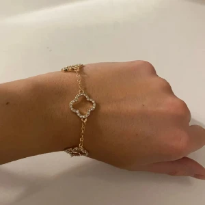Guldarmband med fyrklöverdesign - Säljer ett elegant guldarmband med en unik fyrklöverdesign. Armbandet har flera fyrklöverformade länkar som är dekorerade med gnistrande stenar. Perfekt för att ge en touch av glamour till vilken outfit som helst. Passar både till vardags och fest!