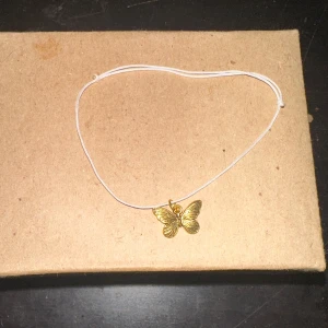 Guld fjärilsarmband - Säljer ett supergulligt armband med en guld fjärilsberlock. Bandet är tunn och vit, vilket gör att fjärilen verkligen står ut. Perfekt för att lägga till en söt detalj till vilken outfit som helst!