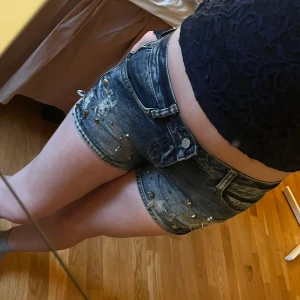 Shorts med detaljer - Blåa lågmidjade jeansshorts med döskallar på framsidan och cool design på bakfickorna💕 Storlek 25 Kom privat för frågor!