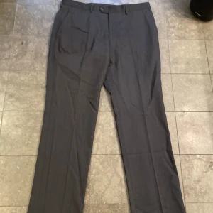 Grå kostymbyxor i ull - Säljer ett par mörkgrå stilrena grå kostymbyxor från Arguments. De är tillverkade i 100% ull. Byxorna har en klassisk straight passform.