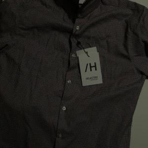 Rutig skjorta från Selected Homme - Säljer en snygg rutig skjorta från Selected Homme i storlek S. Skjortan har en klassisk design med små rutor i vitt, rött och marinblått. Den är slim fit och har långa ärmar med knappar framtill. Perfekt för både vardag och fest!