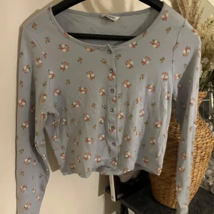 Blommig kofta från Monki - Säljer en superfin ljusblå kofta från Monki med söta blommor över hela. Den har långa ärmar och knappar framtill💙Använd 1 gång, storlek M