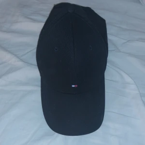 Svart keps med broderad logga - Säljer en stilren svart keps med en liten broderad logga framtill. Kepsen har en justerbar rem baktill för perfekt passform. Perfekt för både vardag och sportiga aktiviteter!