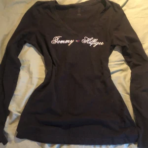 Svart långärmad tröja från Tommy Hilfiger - Säljer en snygg svart långärmad tröja från Tommy Hilfiger. Den har en stilren v-ringning och det klassiska Tommy Hilfiger-loggan broderad. Perfekt för både vardag och lite finare tillfällen. Är lite osäker på storlek men skulle gissa S.