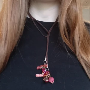 Handgjort halsband  - Handgjort halsband med brunt imiterat mockaband på 1 meter och röda skimrande pärlor och bruna pärlor. Man kan knyta det på olika sätt