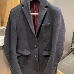 Mörkblå rock från GANT - Säljer en stilren mörkblå rock från GANT i storlek S. Klassisk design med fodrad vinröd insida och tre innerfickor. Jag är 190 lång (75kg) liiite bredaxlad och den har blivit för tajt i axlarna och är kort i armarna på mig. Gott skick. Kostade 4000kr