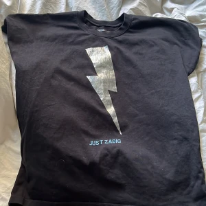 Svart t-shirt från Zadig & Voltaire - Säljer en cool svart t-shirt från Zadig & Voltaire med en stor blixt i silver på framsidan och texten 'JUST ZADIG’. Storlek m men passar också s! Säljer då den inte kommer till användning längre💞💞