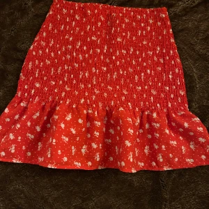 Röd och vitblommig smockkjol  - En smockad blommig kjol med en volang vid botten. Den är i storlek XXS men funkar även för en S och XS. Jättefint skick, går även att använda som en tubtopp om man vill det.