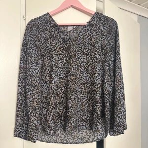 Mönstrad blus från ICHI - Säljer en superfin blus från ICHI med ett coolt leopardmönster i svart och brunt på en ljusblå bakgrund. Blusen har långa ärmar och en avslappnad passform, perfekt för både vardag och fest. Den är gjord i ett lätt och luftigt material som känns skönt mot huden. Perfekt för att piffa upp vilken outfit som helst! 🐆💙