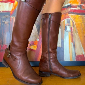 Bruna skinnstövlar med spänne - Säljer ett par snygga bruna stövlar i skinn. De har en dragkedja på insidan och ett stilrent spänne på utsidan. De ger en klassisk look till vilken outfit som helst. Stövlarna är i nyskick och passar bra till både var