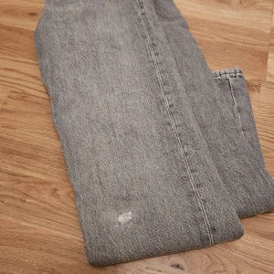 Grå jeans - Säljer ett par grå jeans i normal passform. De har en klassisk femficksdesign och är i ett välanvänt skick med en liten slitagefläck på framsidan. Perfekta för en avslappnad vardagslook! Hål där fram för jag ramla.