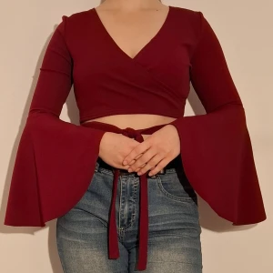 Vinröd crop top med vida ärmar - En vinröd crop top med vida ärmar och knytning fram.   (Sista bilden visar en närbild på materialet av tröjan men färgen stämmer ej)