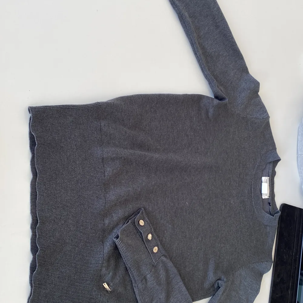 Grå stickad tröja med guldiga detaljer på armarna. Från Lindex/ Holly and white i storlek XS. En liten guld detalj har går av lite men det går att du tillbaka. . Neuletakit & Villapaidat.