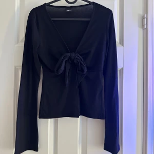 Svart långärmad topp med knyt - Säljer en stilren svart topp med långa ärmar och en snygg knytning framtill. Perfekt för både vardag och fest.😍