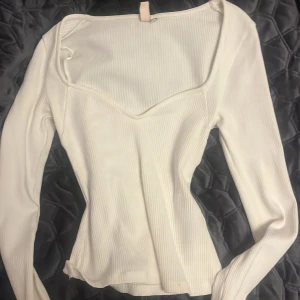 Vit ribbad topp från Nelly - Säljer en stilren vit ribbad topp från Nelly med långärmad design och en elegant v-ringning.