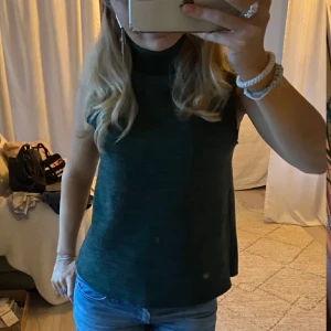 Mörkgrön ärmlös polotopp - Snygg mörkgrön ärmlös polotopp i ett mjukt material. Perfekt för lager-på-lager eller att bära som den är. Enkel och stilren design som passar till många olika outfits. 