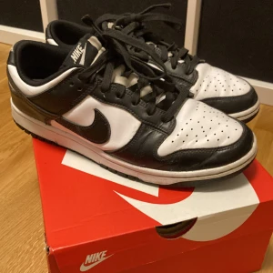 Nike Dunk Low Retro - Säljer ett par Nike Dunk Low Retro i svart och vitt. Skorna har en klassisk design. De här skona är för dig som vill ha en stilren look. De är använda men jag har tagit hand om de väl.
