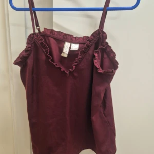 Vinröd linne med volanger H&M 34 - Söt vinröd linne från H&M med smala axelband och volanger. Använd 1 gång. 