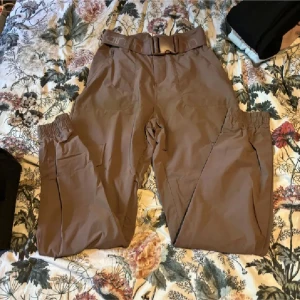 Bruna cargopants med bälte - Snygga bruna cargopants med elastisk midja och praktiska fickor. Byxorna har ett matchande bälte och är perfekta för en avslappnad stil. Tillverkade i ett slitstarkt material.