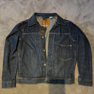 Mörkblå jeansjacka från Levi's Nypris 2’000 - Snygg mörkblå jeansjacka från Levi's med klassisk design och knappar framtill. Jackan har en bröstficka med det ikoniska röda Levi's-märket och en jätte snygg blå färg.              Jackan är oanvänd utan defekter med tag.