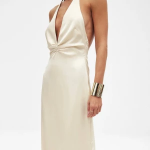Maxiklänning med halterneck - Oanvänd med prislappar kvar. Superfin balklänning med flowy fit och en öppen rygg (dold dragkedja) och en hög slits på baksidan.     Ljusbeige, krämvit, helt slutsåld online Danielle Copperman x NA-KD