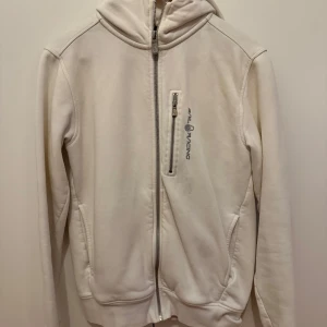 Vit zip hoodie från sail racing - Säljer en stilren zip hooide från sail racing med dragkedja framtill. Knappt använd och i bra skick!