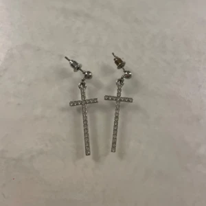 Silvriga kors örhängen - Snygga silvriga örhängen i form av kors, dekorerade med glittrande stenar. Från Ur och Penn. Perfekta för att ge en elegant touch till din outfit!