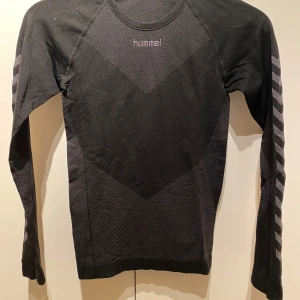 Svart långärmad tröja från Hummel - Säljer en svart långärmad tröja från Hummel med diskreta mönster och logga på bröstet. Tröjan har ett sportigt utseende med mönstrade detaljer på ärmarna. Perfekt för träning eller vardagsbruk. Storlek M/L
