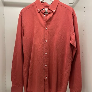 Röd långärmad skjorta - Snygg röd långärmad skjorta med klassisk krage och knappar framtill. Perfekt för en stilren look. Helt oanvänd, kan vara snyggt med en röd färg för att sticka av med resterande vit, blått etc.