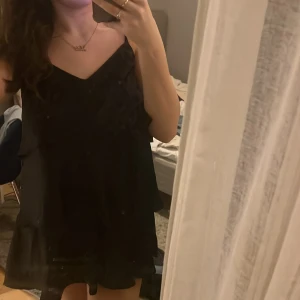 Svart klänning  med volangdetaljer  - Snygg svart kortklänning med tunna axelband och volangdetaljer. Är från Gina och är i jätteskönt ”silkes” material 