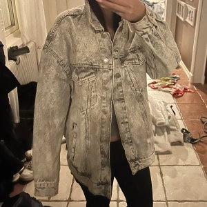 Jeansjacka - Säljer en jeansjacka som är lite grå/vit. Den har knappar vid ärmarna så man kan justera om man vill ha lite större eller mindre.