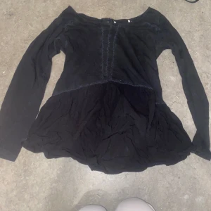 Svart långärmad 2000s topp - Säljer en svart långärmad topp med offshoulder-design. Toppen har en volangdetalj vid nederkanten och är tillverkad i ett mjukt material. Perfekt för en stilren look.