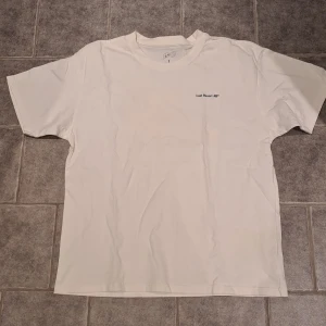 Vit t-shirt från Last Resort AB - Säljer en vit t-shirt från Last Resort AB med tryck på både fram- och baksida. Framsidan har en liten text och baksidan har ett stort grafiskt tryck med texten 'STICK IT TO THE MAN!'. Perfekt för en avslappnad stil. Knappt använd. Storlek L