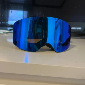 Blå skidglasögon från EQPE - Säljer ett par coola skidglasögon från EQPE med blått spegelglas och svart ram. Justerbart band med vit text för perfekt passform. Perfekta för vinterns äventyr i backen! Använda på en skidresa, nypris 499kr