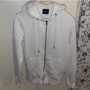 Vit hoodie från Jack & Jones - Säljer en stilren vit hoodie från Jack & Jones. Den har en dragkedja framtill och justerbar huva med snören. Perfekt för en avslappnad look. Priset är ej hugget i sten vilket innebär att vi kan förhandla lite med priset 😊