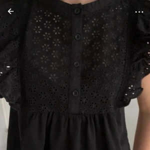 Svart blus med spetsdetaljer - Snygg svart blus med spetsdetaljer och knappar framtill. Blusen har volangärmar och ett vackert blommönster i spetsen. I nyskick, pris kan diskuteras💞💞