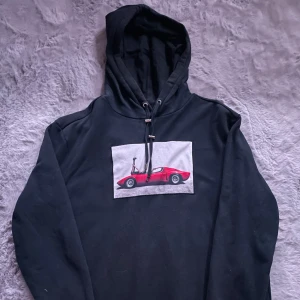 Limitato hoodie - Snygg svart hoodie från Riocam med ett coolt tryck av en röd sportbil på framsidan. Perfekt för dig som gillar unika och stilrena plagg. Hoodien har en klassisk passform med dragsko i huvan.