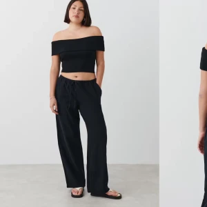 Svart offshoulder topp Gina - Snygg svart offshoulder topp med croppad passform. Perfekt för en stilren look, denna topp är både trendig och bekväm. Den har en bred kant upptill som ger en elegant touch.