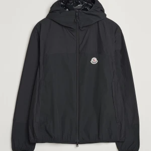 Moncler Kona, Svart vindjacka från Moncler - Köpt på CareOfCarl, kvitto medföljer. Snygg svart vindjacka från Moncler med dragkedja och huva. Perfekt för blåsiga dagar. Jackan har en stilren design med Moncler-logga på bröstet.