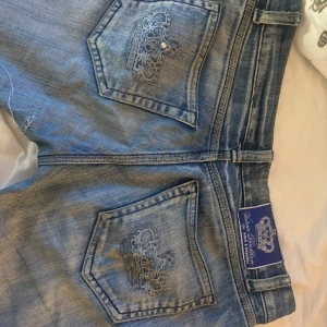 Blå jeans med broderad detalj - Snygga blå jeans med broderade detaljer på bakfickorna. Klassisk femficksdesign med knapp och dragkedja framtill. Perfekta för en avslappnad stil. Låg midjade. Ett hål fins mellan benen men det är ihop sytt 