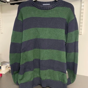 Randig stickad tröja från Brandy Melville - Säljer en mysig stickad tröja från Brandy Melville i grönt och blått. Tröjan har ett randigt mönster och långa ärmar, perfekt för kyligare dagar. Den är i en bekväm passform och har en rund halsringning.