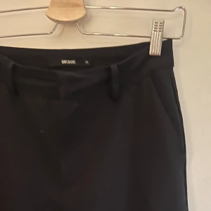 Svarta kostymbyxor från Bik Bok - Snygga svarta byxor från Bik Bok med en klassisk design. De har en bootcut passform och är perfekta för en stilren look. Byxorna har hällor för bälte och diskreta fickor baktill. Obs högmidjade