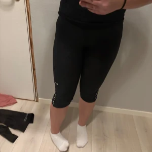 Svarta träningsleggings från Nike - Säljer ett par svarta träningsleggings från Nike med Dri-FIT-teknologi. De är knälånga och har en tight passform, perfekt för träning. Diskret Nike-logga på benet.