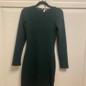 Mörkgrön klänning från H&M - Elegant mörkgrön klänning från H&M med långärmad design och en stilren öppen ryggdetalj. Perfekt för en chic look.