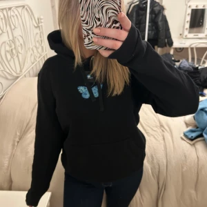 Svart hoodie med blå fjäril från The Cool Elephant - Säljer en svart hoodie från The Cool Elephant med en stor blå fjäril på ryggen och en mindre på framsidan. Hoodien har långa ärmar och en mysig huva. Perfekt för en avslappnad stil.