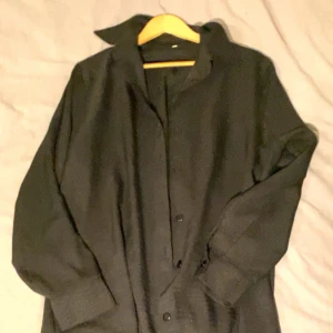 Svart kappa med knappar - Elegant svart kappa med knappar och långa ärmar. Perfekt för en stilren look under kyligare dagar. Den har en byxa som är svart så det är ett set tillsammans.